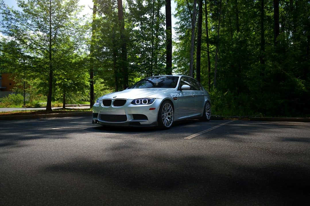 silver BMW sports sedan parked in an empty parking lot surrounded by tall green trees