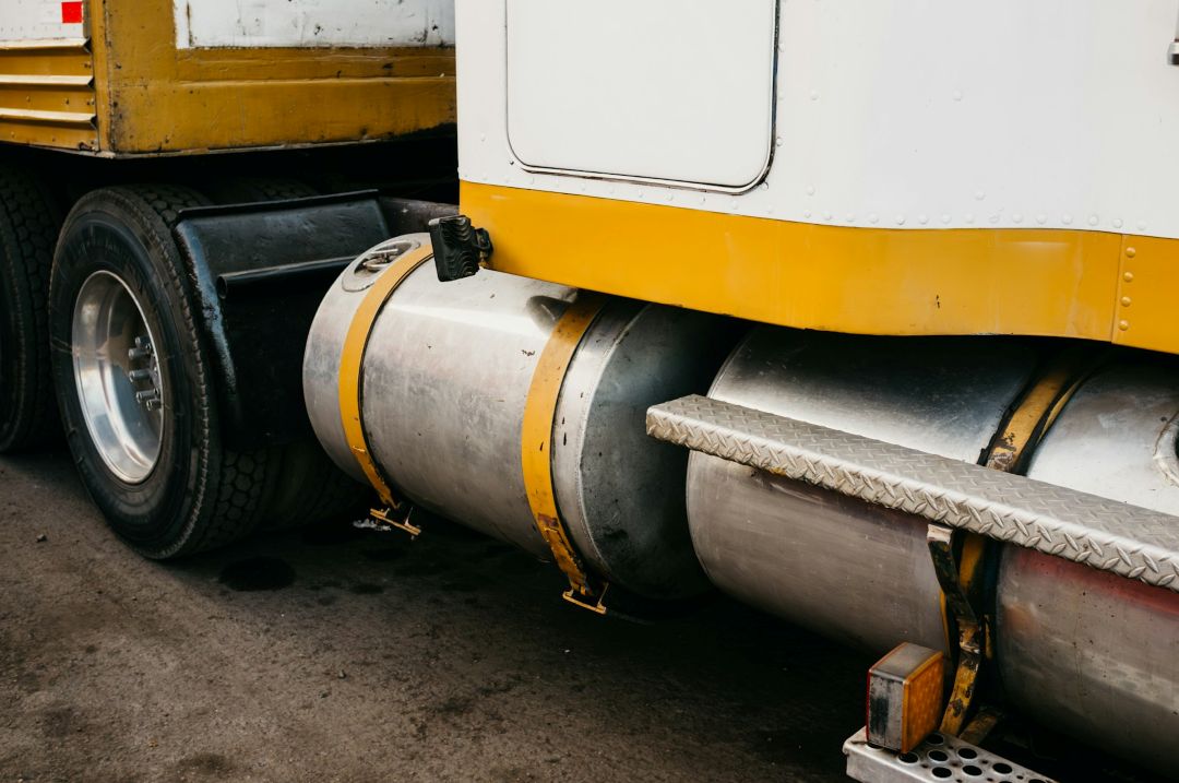 A yellow and white semi-truck underside showing cylindrical aluminum fuel tanks