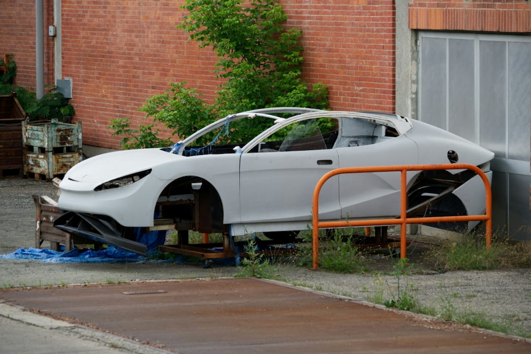 partially dismantled car shell left outside near a brick building, with major components removed