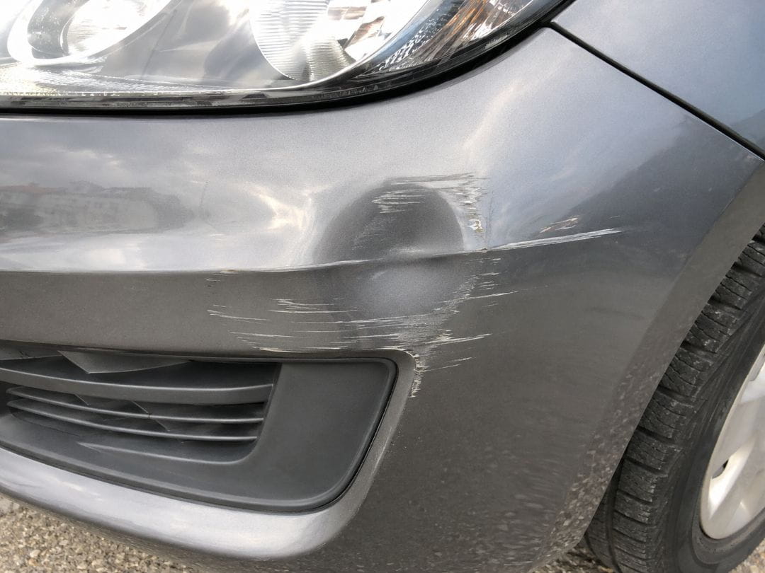 close-up of white scuff marks and scratches on the front bumper of a gray car
