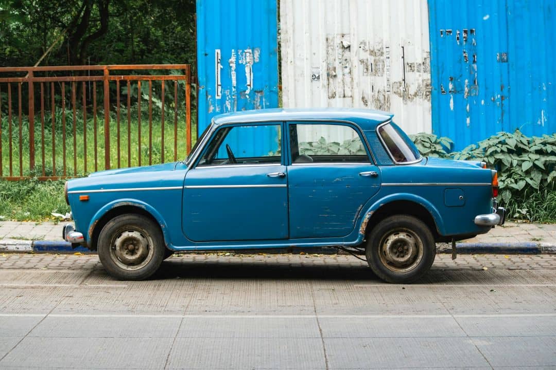 side view of an old blue vintage sedan with worn paint and rust around the wheel arches