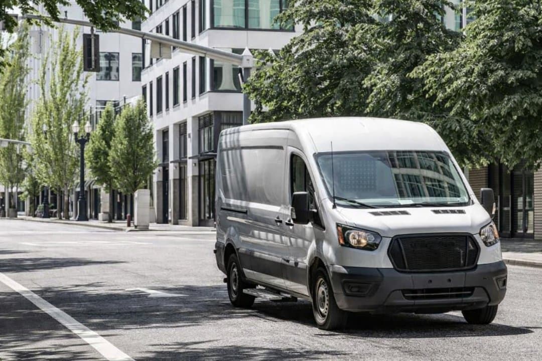a white commercial cargo van driving on a quiet city street