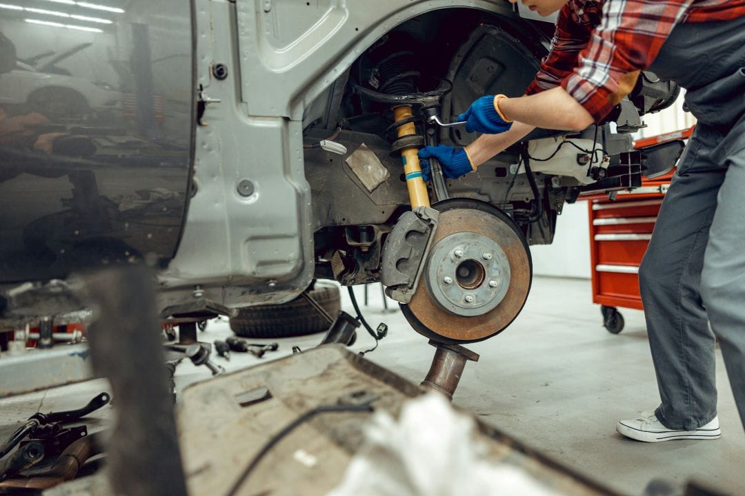 mechanic repairing a car suspension and brake assembly on a partially dismantled vehicle