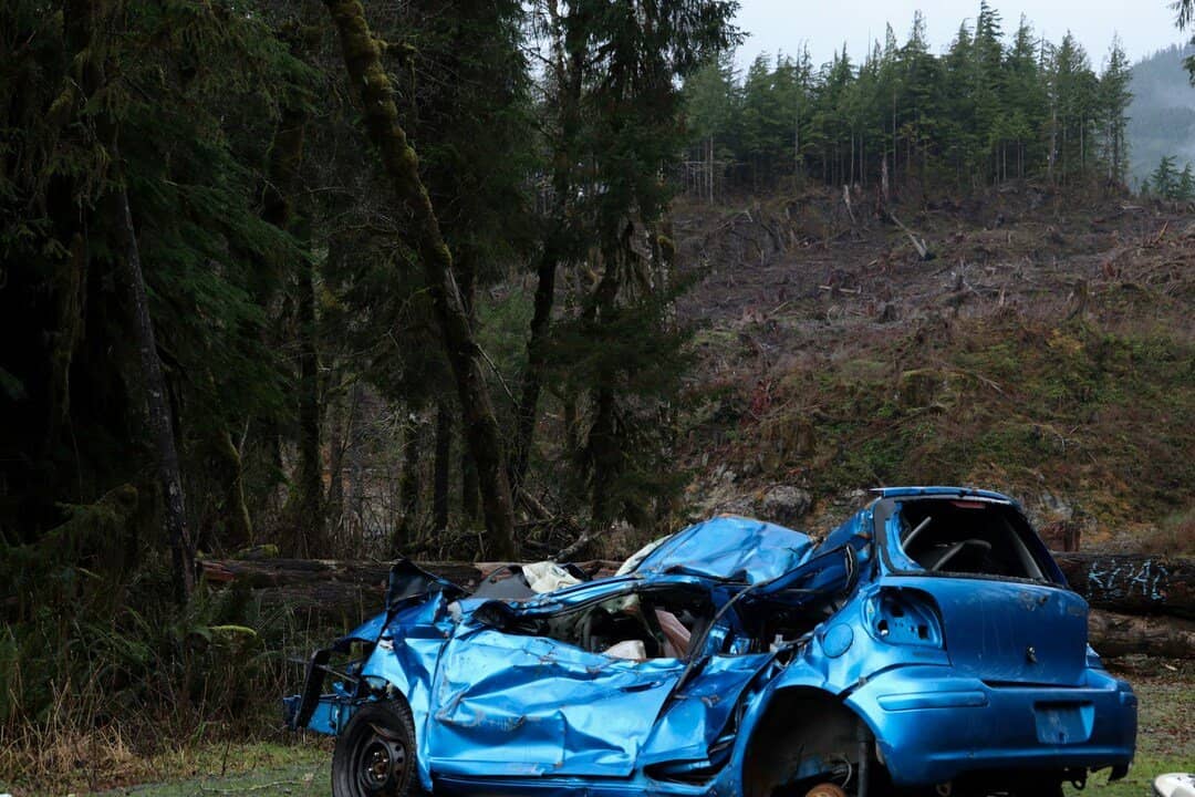 severely damaged blue car with a crushed front end, collapsed roof, and shattered windows