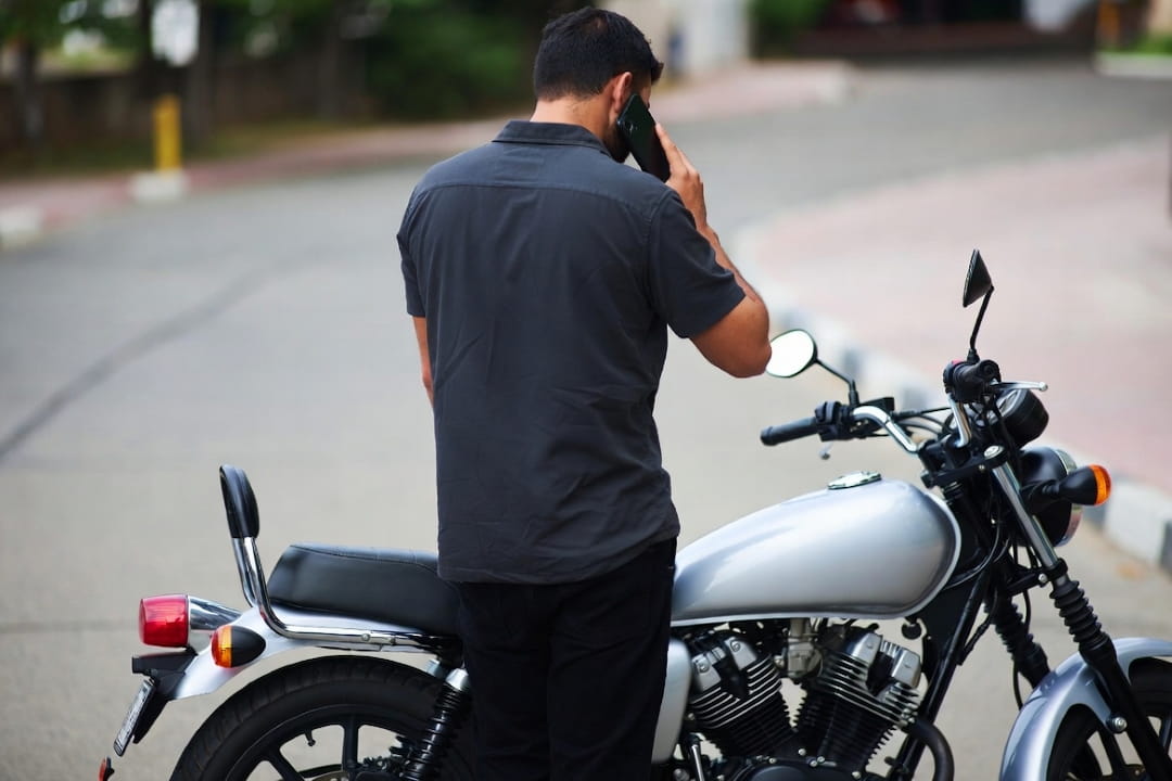 Un hombre haciendo una llamada telefónica junto a una motocicleta estacionada