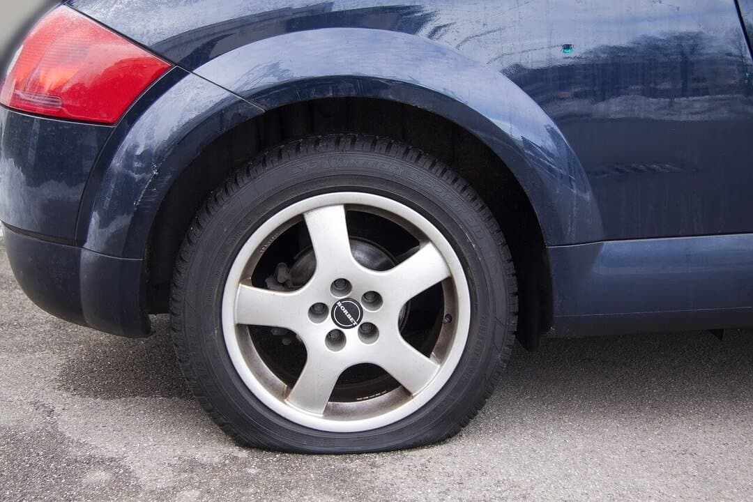 close-up of a flat car tire with a silver alloy wheel on a dark blue vehicle parked on pavement