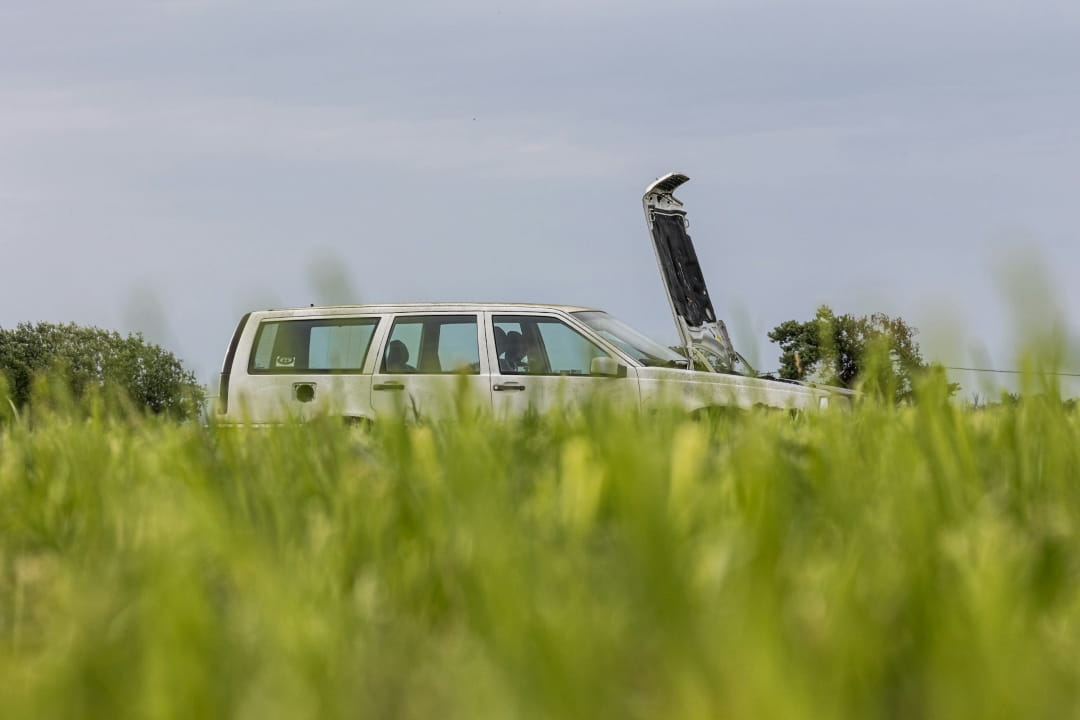 vehicle with an open hood parked in tall grass, suggesting mechanical trouble