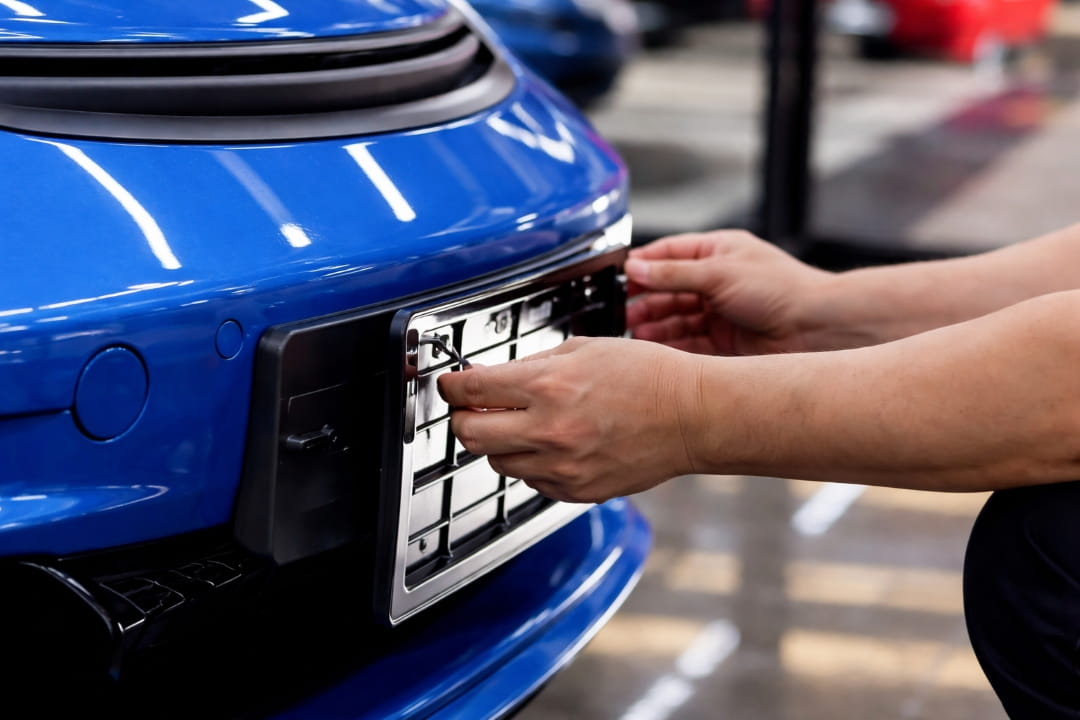 a person installing or removing a license plate frame on the front of a blue car