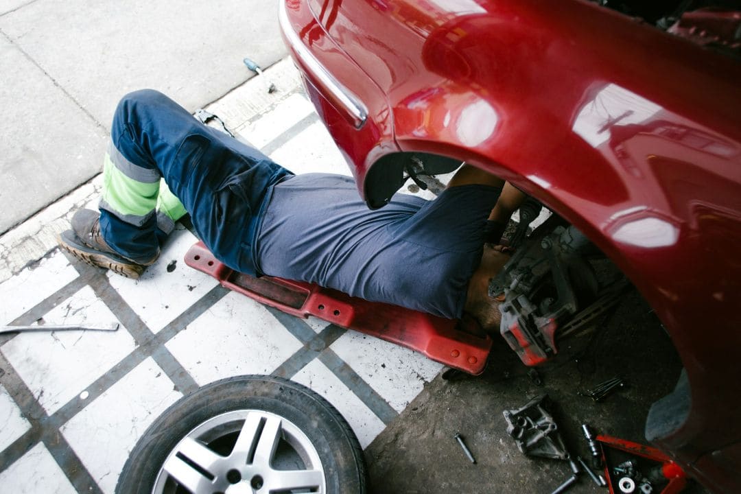 mechanic working underneath a red car in a garage