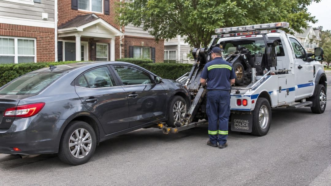 tow truck operator loading a gray sedan outside a residential building