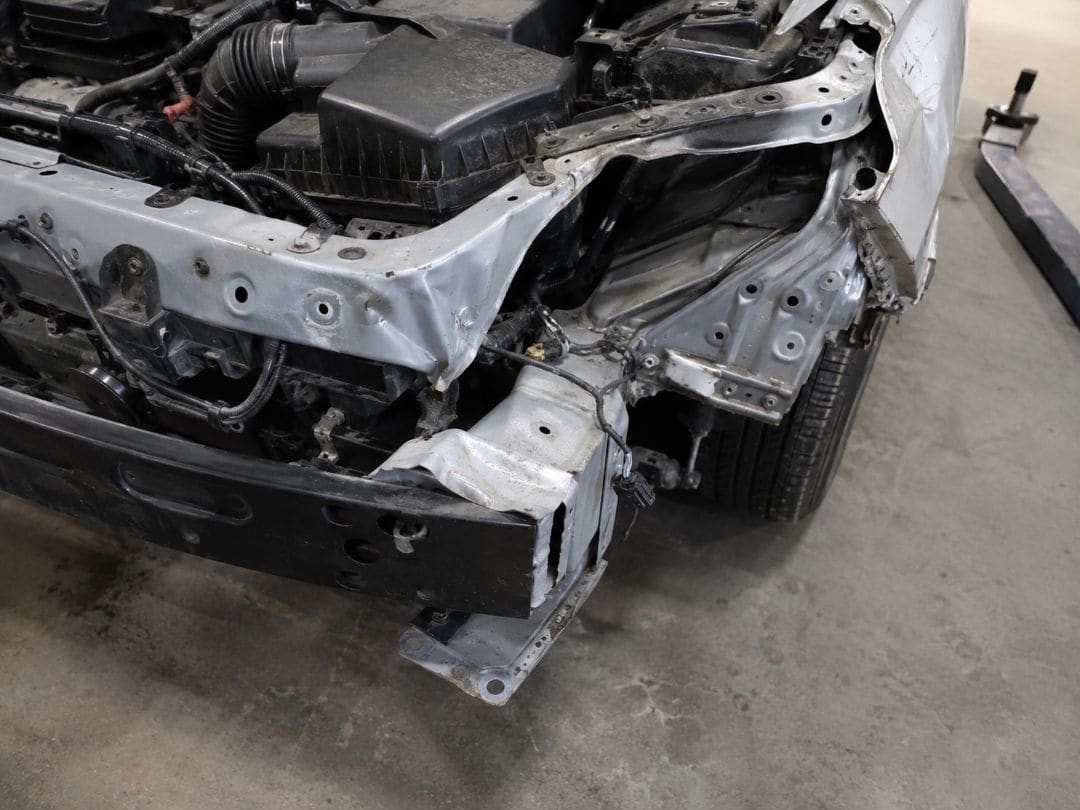 close-up of severe front-end frame damage with bent structural supports and exposed engine components