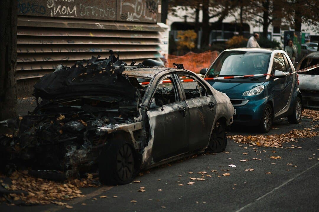 severely burned-out car with a charred body and destroyed roof parked on a city street