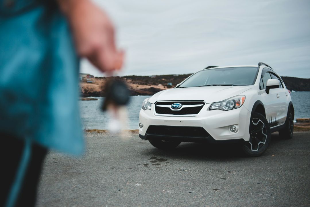 person holding car keys beside a white used SUV parked near the coast