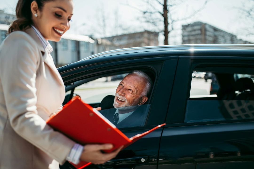 car salesperson speaking with a smiling customer seated in a used car