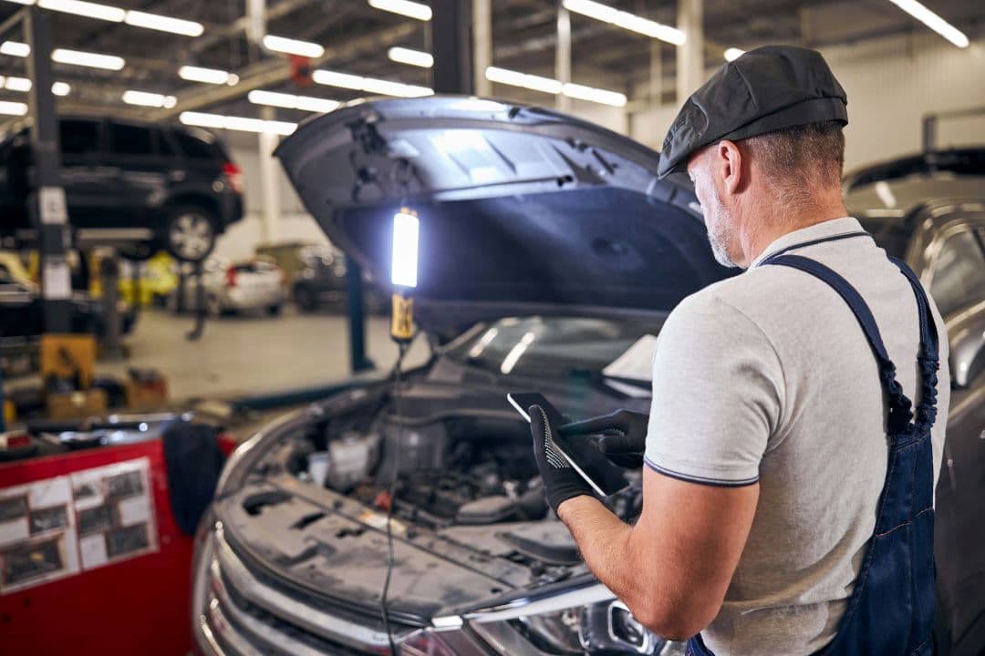 mechanic performing a pre-purchase inspection on a car with the hood open in an auto repair shop