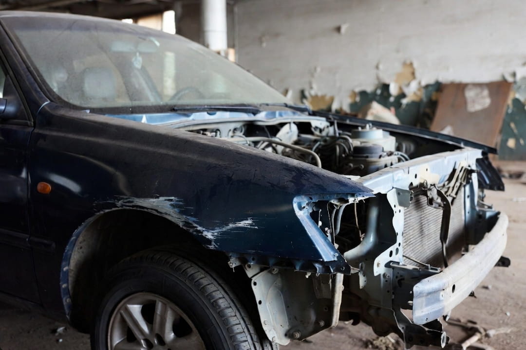 front-end view of a damaged car with missing bumper and exposed engine components